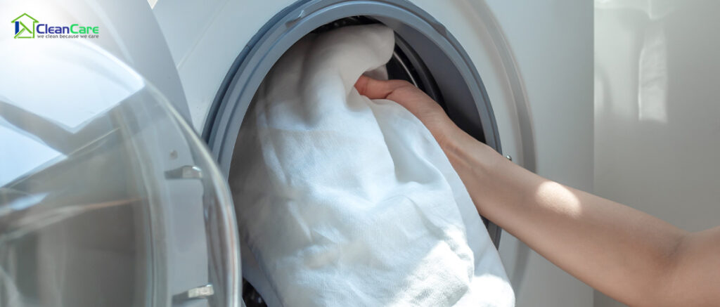 Hand putting laundry into a washing machine.