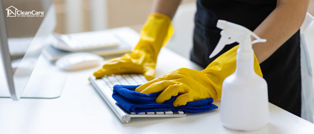Person sanitizing a keyboard with a spray bottle and cloth.